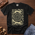 A black graphic t-shirt featuring a cream-colored print of a hare, a fox, and a tree stump, styled in a flat-lay on a wooden surface with mushrooms, a leather bag, and blue jeans.